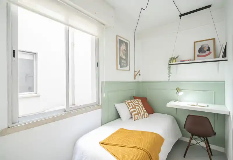 Bright, compact single bedroom with a neatly made bed, cozy textiles and a small built-in desk by the wall — ideal for a student or short-term stay.