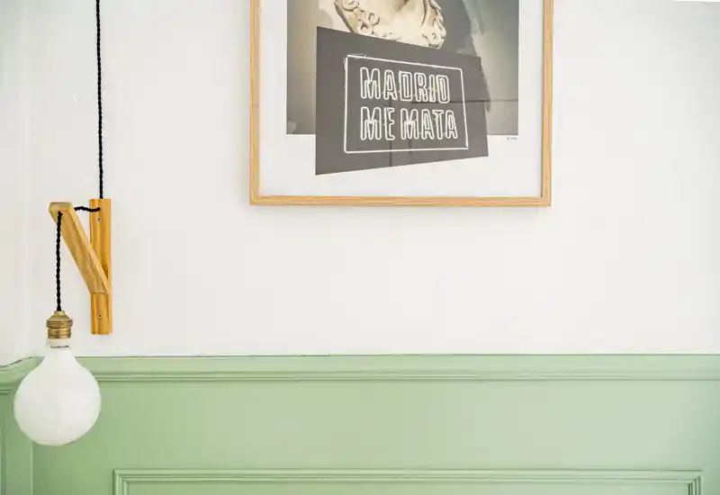 Detalle interior con friso verde menta, un cuadro enmarcado y una bombilla colgante: una escena decorativa, no una vista completa de una habitación.