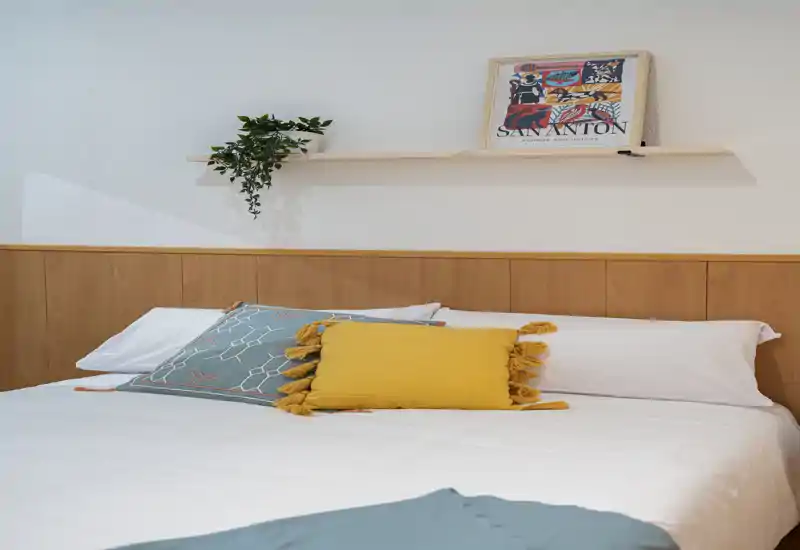 Bright, well-staged bedroom with a neatly made double bed, decorative cushions and a minimalist shelf with artwork — ideal for a cozy rental listing.
