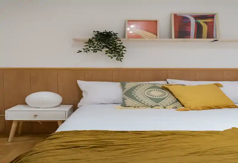 Bright, styled bedroom with a wooden headboard, decorative cushions and a mustard throw—clean, cozy and ready for a listing photo.