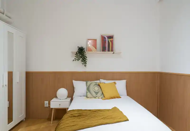 Bright, neatly styled bedroom with a double bed, warm wooden paneling and decorative cushions; ideal for a cozy short-term rental.