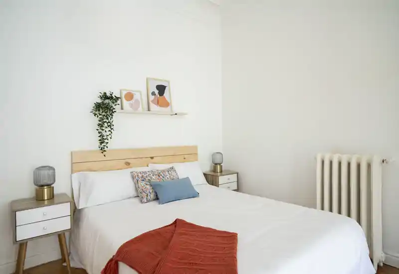 Bright, minimal bedroom with a wooden headboard, bedside tables and decorative cushions on a neatly made bed — ideal for holiday rentals or listings.