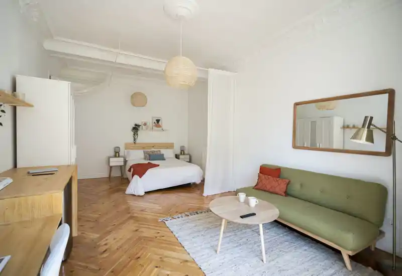 Bright, stylish bedroom-studio with a comfortable double bed, wooden parquet floor and a cozy sitting area with sofa and coffee table — ideal for a relaxed city stay.