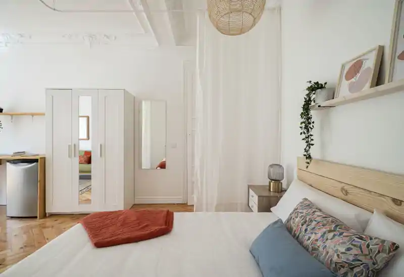 Bright, stylish bedroom with a neatly made bed, patterned cushions and warm wooden details; soft natural light and tasteful decor create a welcoming atmosphere.