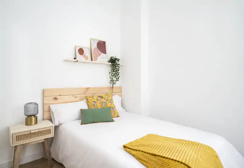Bright, minimalist bedroom with a wooden headboard, decorative pillows and a cosy mustard throw — ideal for relaxing stays.