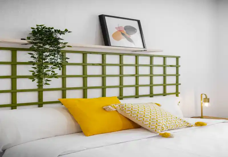 Bright, stylish bedroom shot featuring a neatly made bed with yellow accent pillows, a decorative headboard and a bedside lamp—ideal for listings highlighting cozy modern rooms.