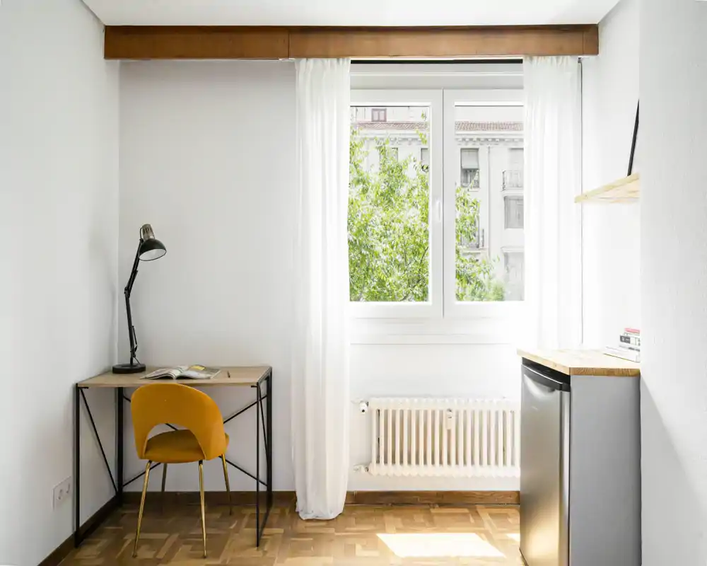 Pièce lumineuse et minimaliste avec un petit bureau et une chaise jaune près de la fenêtre; idéale pour un studio compact ou un espace de travail éclairé naturellement.