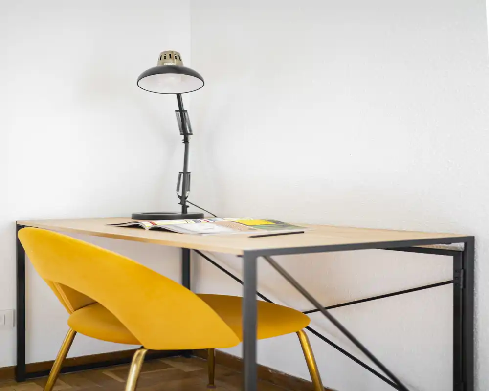 Coin bureau lumineux avec un bureau minimaliste, une chaise jaune vive et une lampe de bureau réglable — idéal pour lire ou télétravailler.