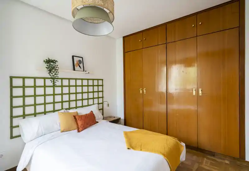 Chambre lumineuse et soignée avec un lit double confortable, de grands placards en bois et des coussins décoratifs pour une ambiance chaleureuse.