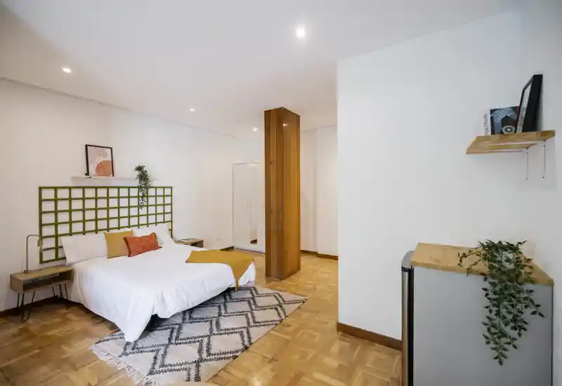 Camera da letto luminosa e moderna con letto matrimoniale, tappeto geometrico e pavimenti in legno; arredo minimale e illuminazione piacevole.