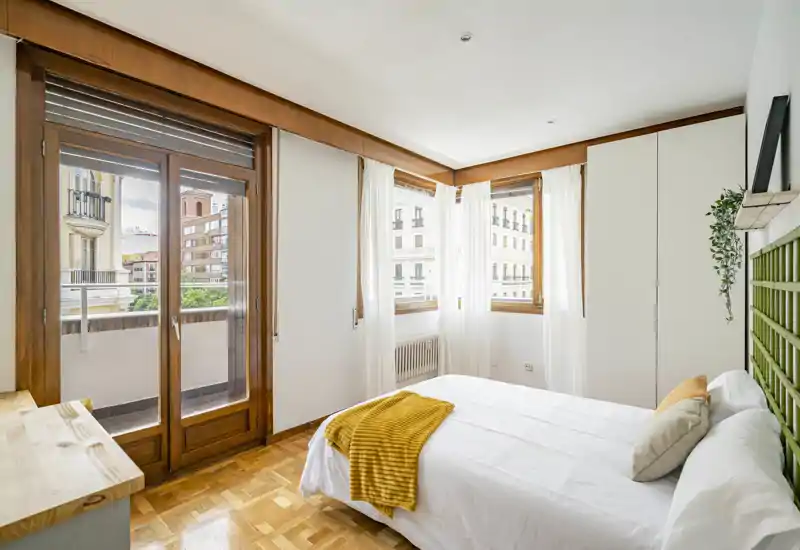 Camera da letto luminosa e ben arredata con letto matrimoniale comodo, biancheria morbida e dettagli caldi; ampie finestre e porta sul balcone garantiscono molta luce naturale.