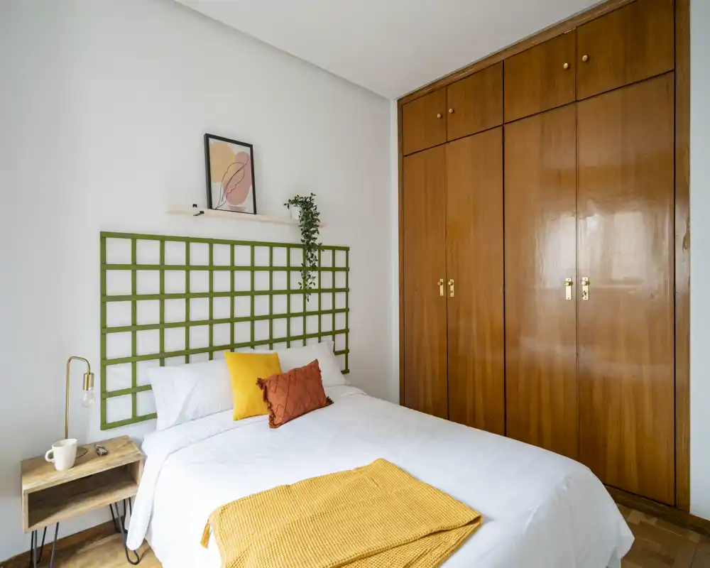 Chambre lumineuse et bien décorée avec lit complet, grands placards en bois et coussins d'accent créant une ambiance chaleureuse et moderne.