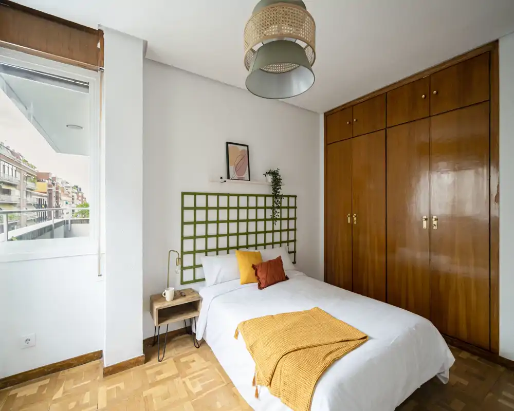 Chambre lumineuse et soignée avec lit double, coussins décoratifs, grande armoire en bois et fenêtre donnant sur un balcon — idéale pour des annonces mettant en avant le confort et la lumière naturelle.