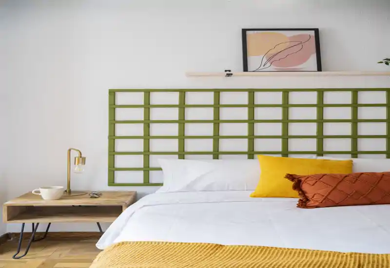 Chambre lumineuse et élégante avec lit blanc, coussins moutarde et rouille, plaid texturé et table de chevet en bois moderne — un espace chaleureux et bien éclairé idéal pour les photos d'annonce.
