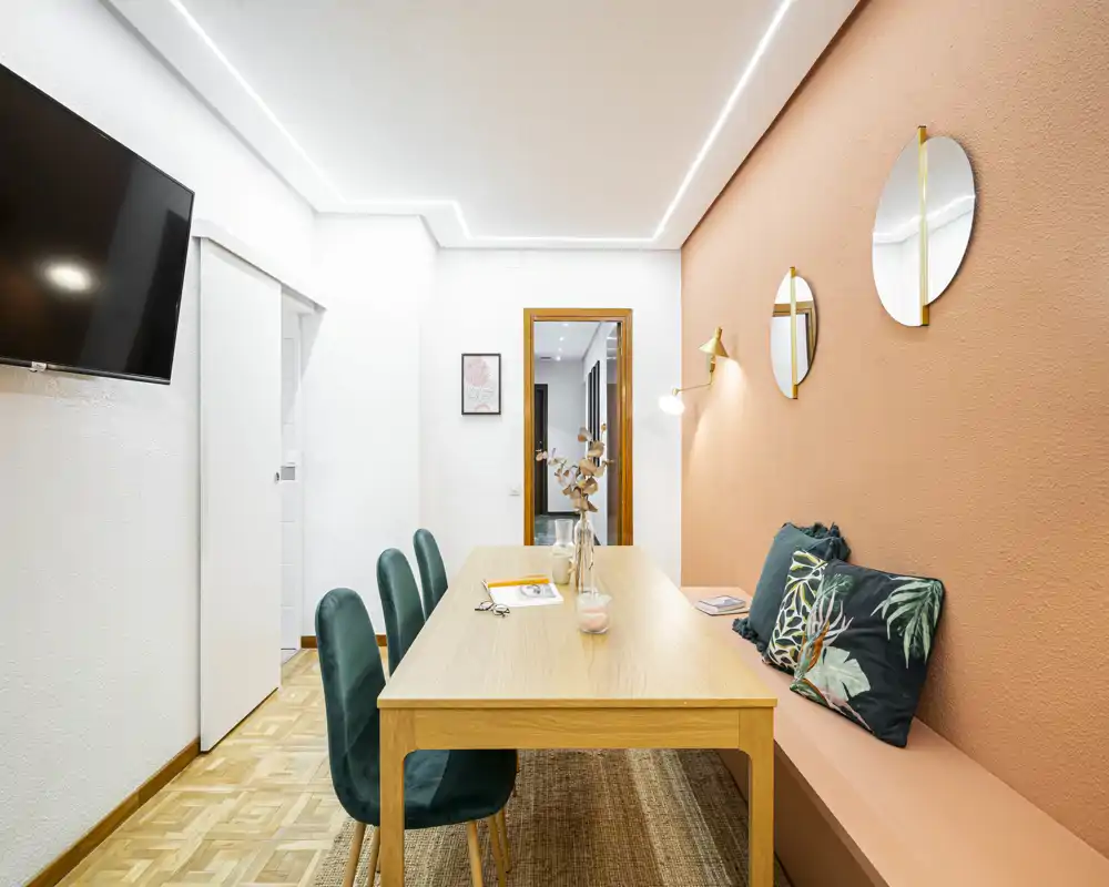 Stylish dining area with a wooden table, emerald velvet chairs and a built-in bench against a warm terracotta wall — well lit and tastefully decorated.