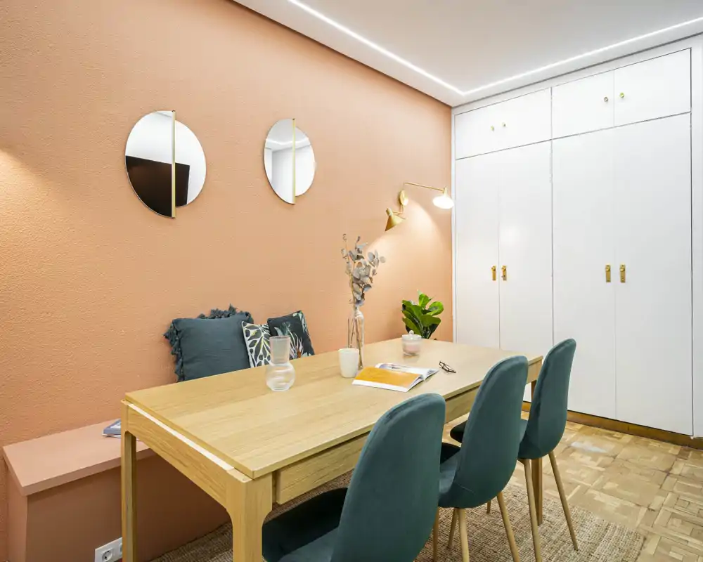 Stylish dining area with a light wood table, velvet green chairs and warm terracotta accent wall — bright, cozy and well styled for comfortable meals.