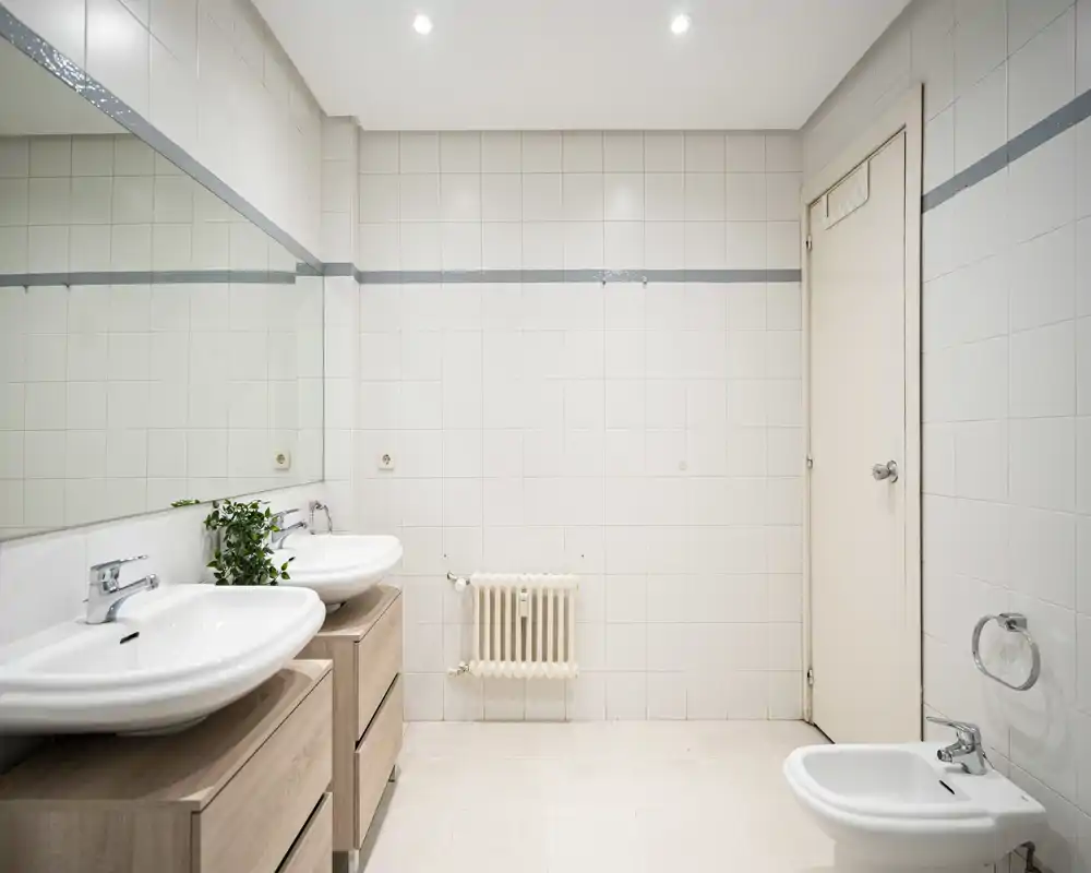 Clean, modern bathroom with twin sinks, large mirror and a bidet. Bright neutral tiles and minimalist wooden vanity create a fresh, functional space.