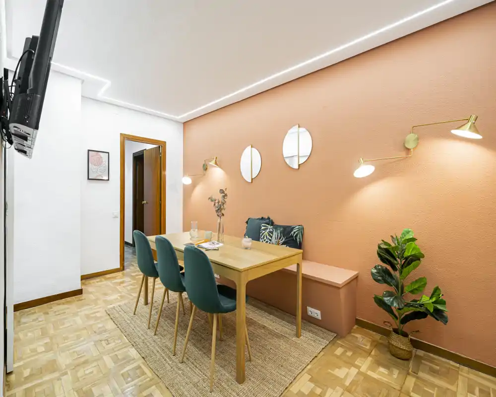 Stylish dining area with a wooden table, four teal chairs, textured rug and warm coral accent wall, ideal for meals and small gatherings.