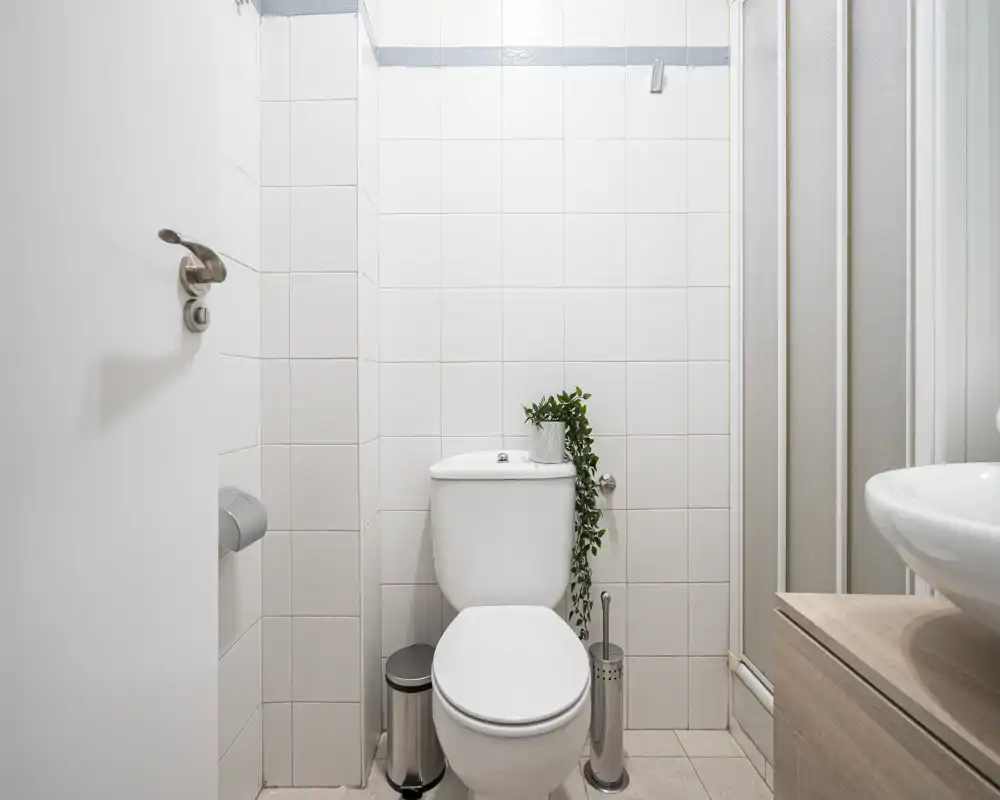 Clean, compact bathroom featuring a toilet, tiled walls, a small shower enclosure and a modern sink partially visible on the right.