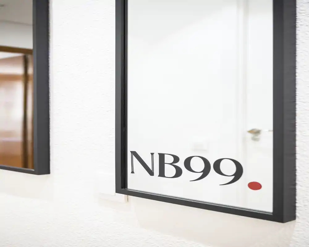 Close-up of a wall mirror with the label 'NB99' printed on the glass; no clear room-specific furniture or layout is visible.