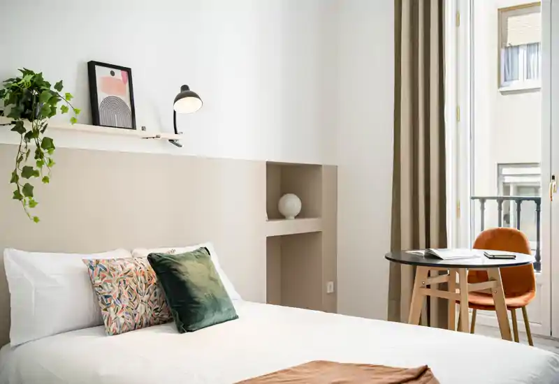 Dormitorio luminoso y con estilo, con cama doble bien hecha, cojines decorativos, un pequeño escritorio junto a la ventana y una decoración moderna y acogedora — ideal para alquileres vacacionales.