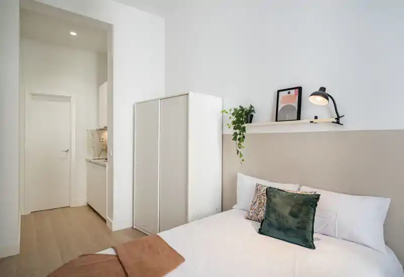 Camera da letto luminosa e minimal con un comodo letto matrimoniale, cuscini decorativi e un armadio compatto — perfetta per soggiorni brevi e accoglienti.