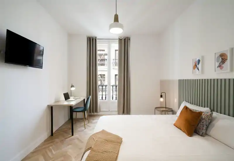 Dormitorio moderno y luminoso con cama doble bien hecha, cojines decorativos y un pequeño escritorio junto a la ventana — ideal para descansar y teletrabajar.