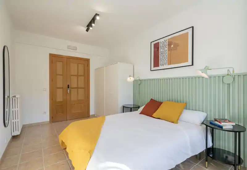 Bright and cozy bedroom with a neatly made double bed, headboard, bedside tables and soft textiles — well lit and welcoming for guests.