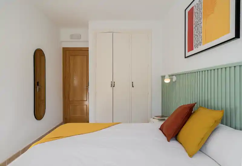 Bright, modern bedroom with a visible bed, headboard and bedside lamp; simple decor and warm accent textiles.