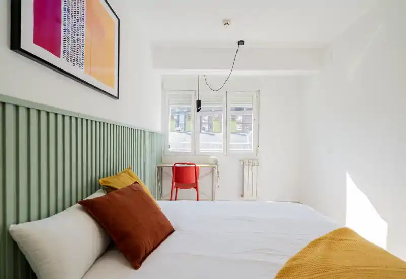 Bright, modern bedroom featuring a neatly made bed with decorative pillows and a warm accent throw; clean white walls and contemporary lighting complete the composition.