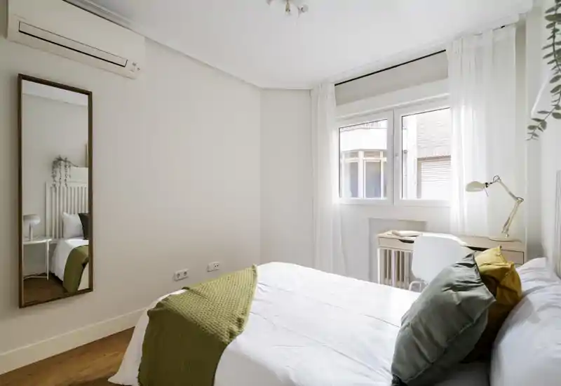 Camera da letto luminosa e minimal con letto matrimoniale ben rifatto, tessili morbidi e una piccola scrivania vicino alla finestra che offre luce naturale — ideale per soggiorni rilassanti o lavoro da casa.