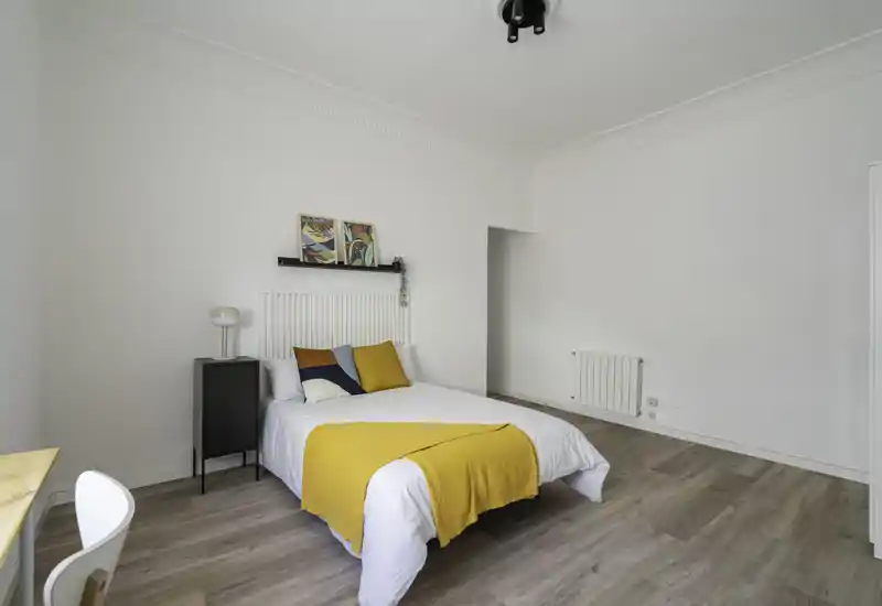 Bright, modern bedroom with a neatly made double bed, warm yellow accents and minimal Scandinavian-style decor — ideal for a vacation rental.
