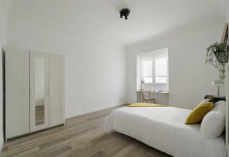 Bright, minimal bedroom with a neatly made double bed, warm accent pillows and a small desk by the window — ideal for peaceful stays or work-from-home guests.