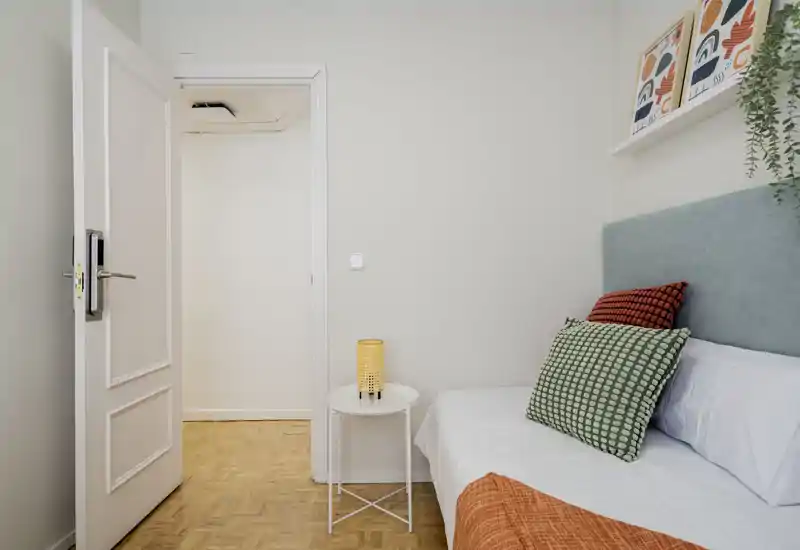 Dormitorio individual luminoso y bien decorado con cabecero azul, cojines estampados y una mesita con lámpara cálida — estilo moderno y acogedor, ideal para anuncios de alquiler.