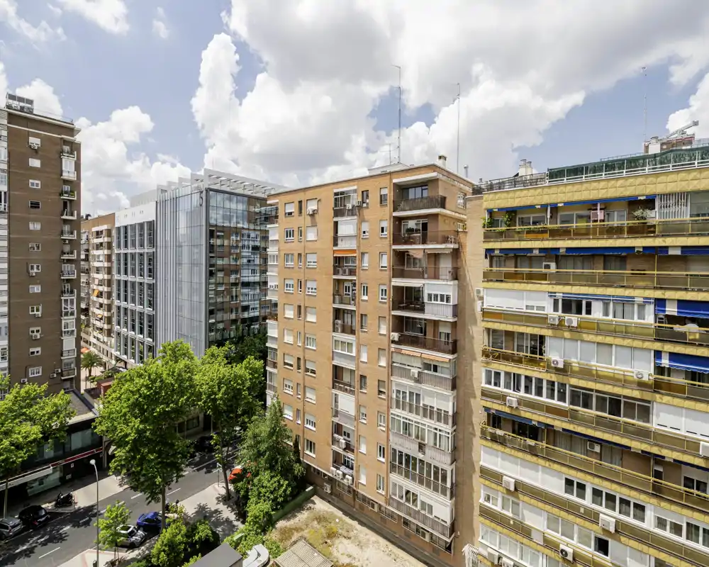 Exterior view of a residential city block with mid-rise apartment buildings, street trees and blue sky — ideal to show the neighbourhood and building facade.