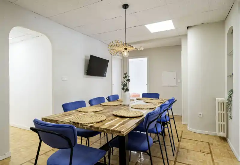 Amplio comedor con una gran mesa de madera y ocho sillas tapizadas en azul, decorado con individuales trenzados y un jarrón central — luminoso, moderno y listo para comidas compartidas.