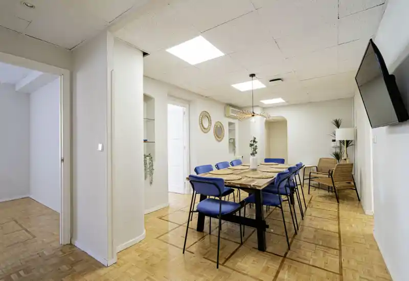 Amplio comedor moderno con gran mesa de madera, sillas tapizadas en azul y detalles en ratán — ideal para comidas en grupo.