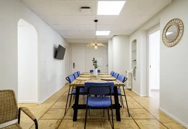 Comedor moderno y luminoso con una larga mesa de madera para seis, sillas azules y una lámpara colgante decorativa — ideal para comidas en grupo.