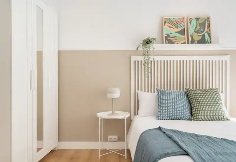 Dormitorio luminoso y moderno con cabecero de listones, cojines estampados y ropa de cama suave. Tonos neutros y decoración sencilla que crean un ambiente tranquilo y acogedor, perfecto para alquileres.
