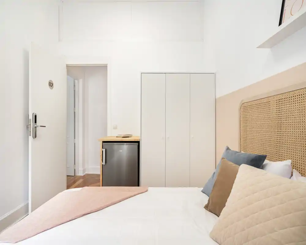 Chambre lumineuse et accueillante avec tête de lit en cannage, coussins superposés et lit bien fait — idéale pour des annonces mettant en avant le confort et un style minimal contemporain.