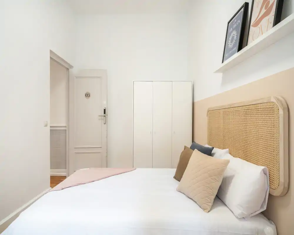 Chambre lumineuse et minimaliste avec une tête de lit en rotin, lit double bien fait et une armoire blanche simple — palette neutre et textiles doux pour une ambiance chaleureuse.