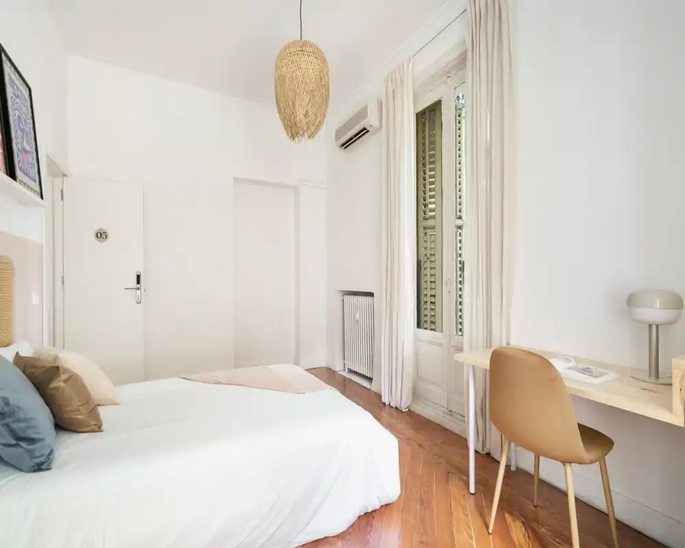 Chambre lumineuse et minimaliste avec lit double, parquet, bureau près de la fenêtre et décoration neutre—parfaite pour un séjour reposant.