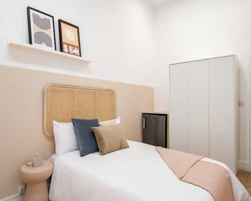 Chambre lumineuse et chaleureuse avec tête de lit en rotin, linge de lit doux et coussins décoratifs ; armoire et table de chevet présents — idéale pour un séjour confortable.
