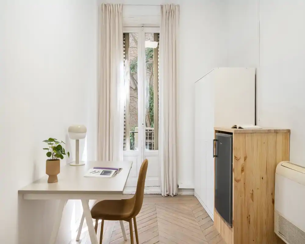 Pièce lumineuse et minimaliste avec un bureau près d'une grande fenêtre, parquet en chevron et rangements compacts — idéale pour un petit bureau ou un coin de vie.