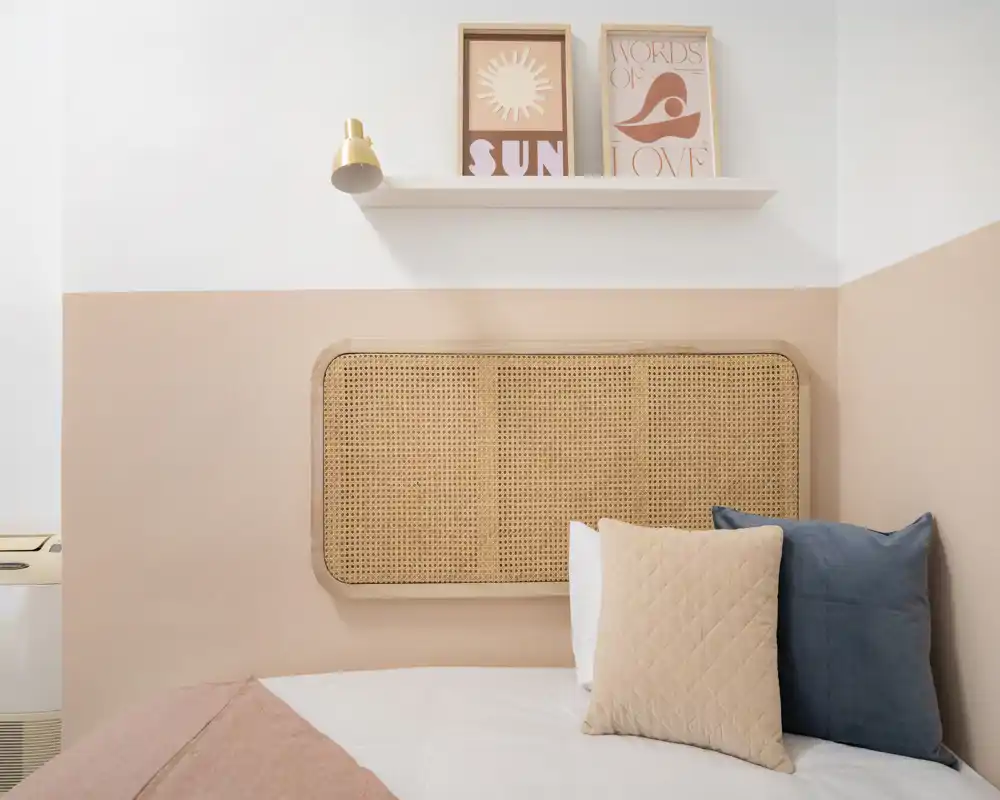 Coin chambre lumineux et chaleureux avec une tête de lit en rotin tressé, coussins doux et tons pastel chaleureux — idéal pour un séjour calme et stylé.