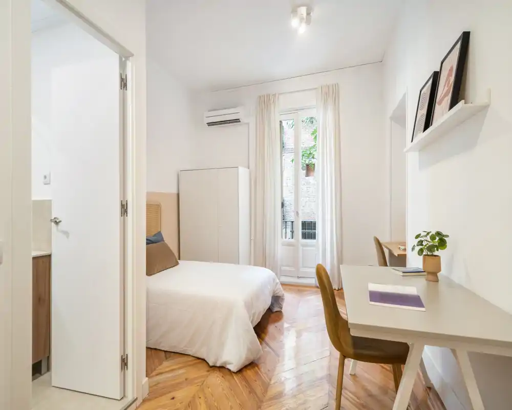 Chambre lumineuse et élégante avec lit double, parquet point de Hongrie et bureau près de la fenêtre. Murs blancs et textiles doux offrent une ambiance chaleureuse idéale pour la location touristique.