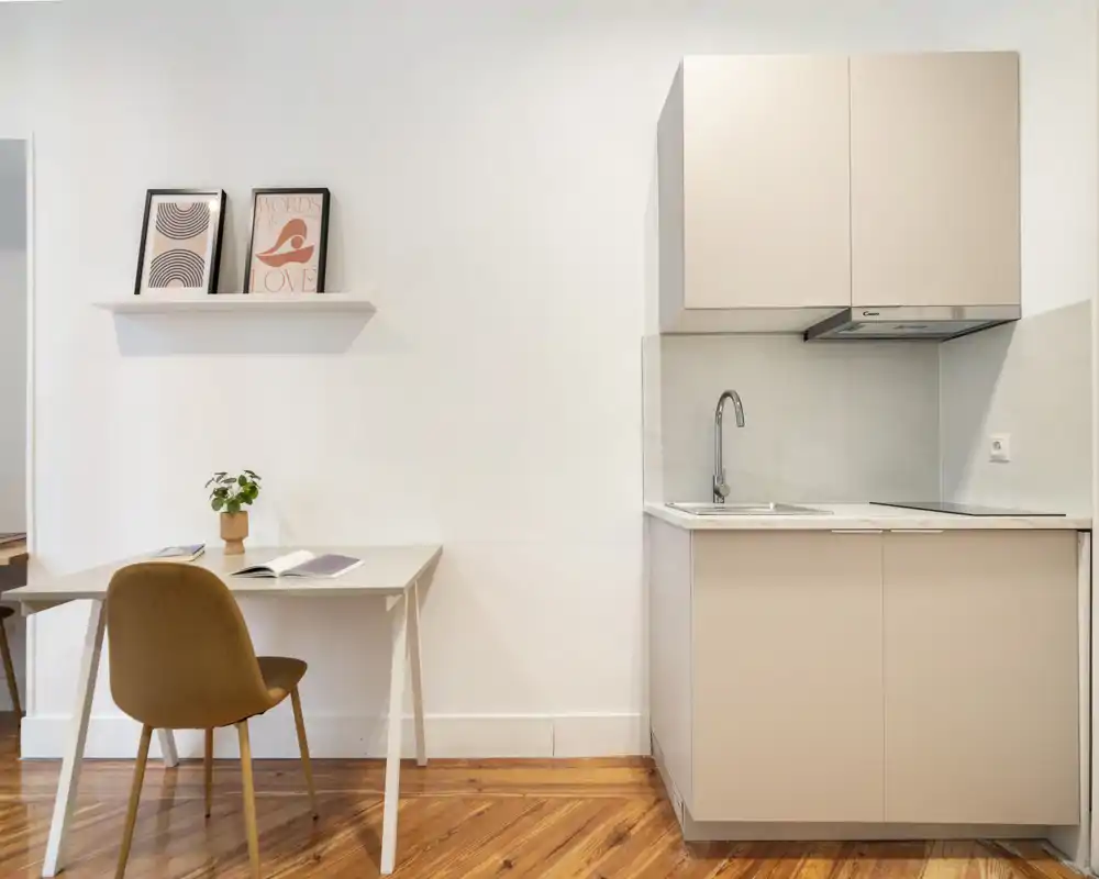 Kitchenette compacte et moderne avec meubles neutres, plan de travail effet marbre, hotte intégrée et petite table de travail avec chaise — lumineuse, soignée et au style doux, parfaite pour un studio.