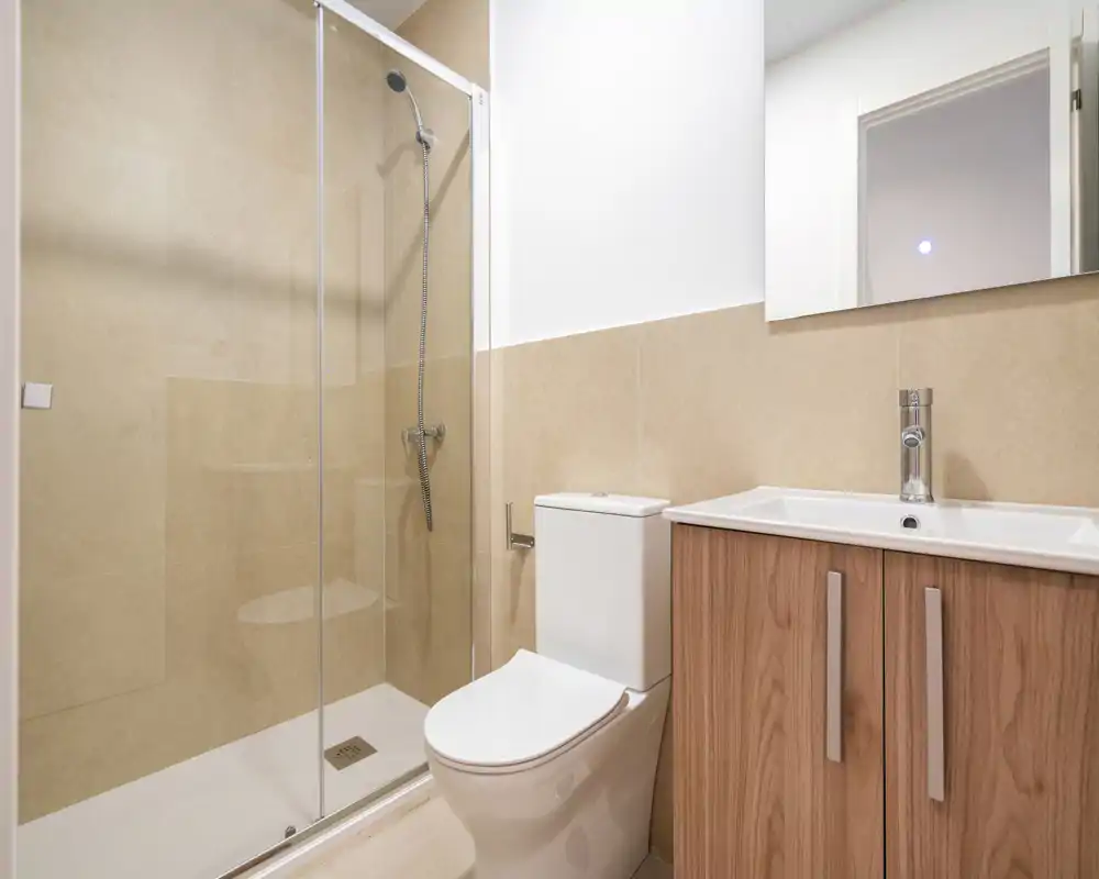 Salle de bains moderne et lumineuse avec douche vitrée, WC et meuble vasque en bois avec miroir — design propre et contemporain, idéal pour les annonces locatives.