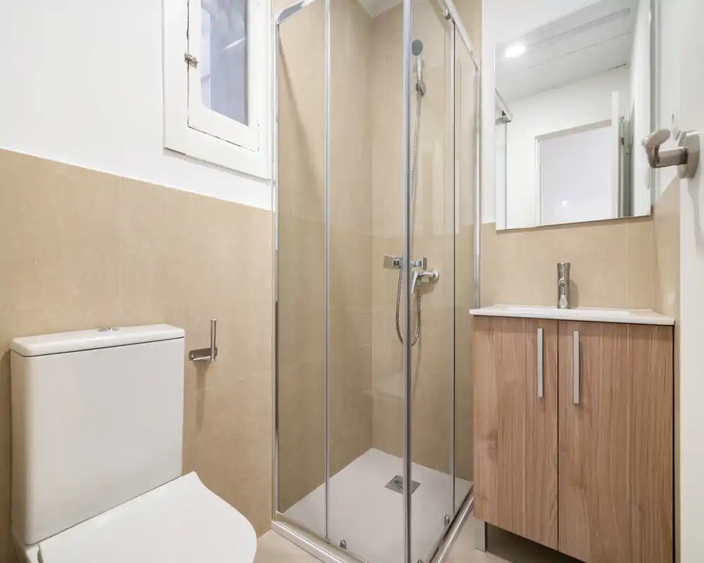 Salle de bains moderne et lumineuse avec cabine de douche d'angle, toilettes et meuble vasque en bois — carrelage neutre et grand miroir pour agrandir l'espace.