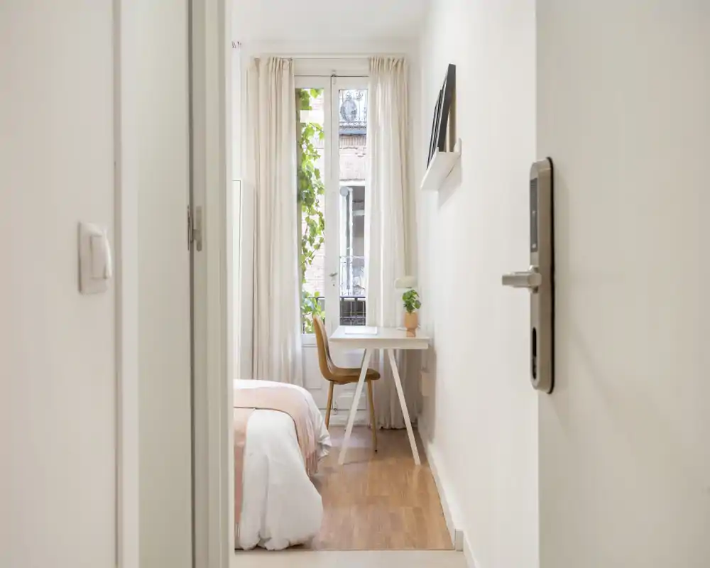 Chambre lumineuse et chaleureuse avec linge de lit doux, un petit bureau près de la fenêtre et une belle lumière naturelle — idéale pour se détendre ou télétravailler.
